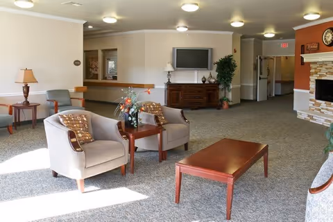 Sunny senior living facility common room with armchairs, a coffee table, TV console and a fireplace.