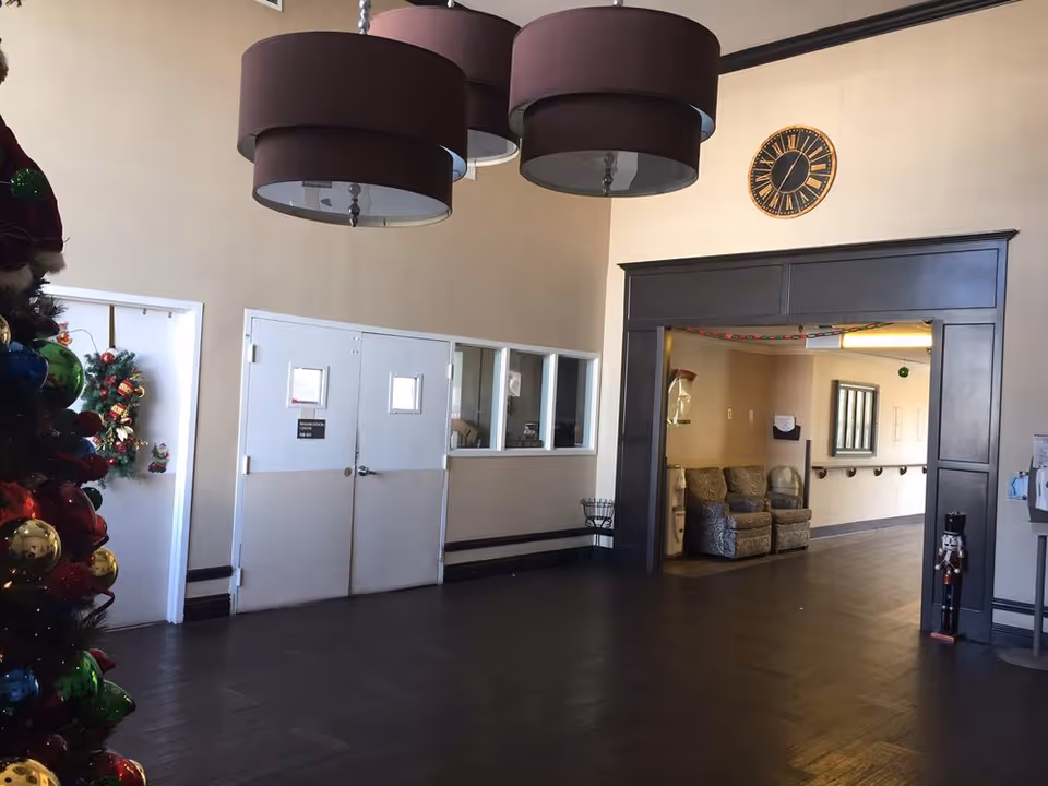 Spacious lobby with large round pendant lights, a decorated Christmas tree, double doors and seating visible through an open doorway.