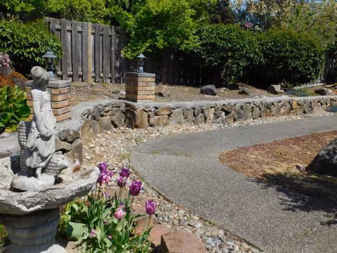 Stone fountain statue, winding path, and blooming tulips in a landscaped outdoor garden.