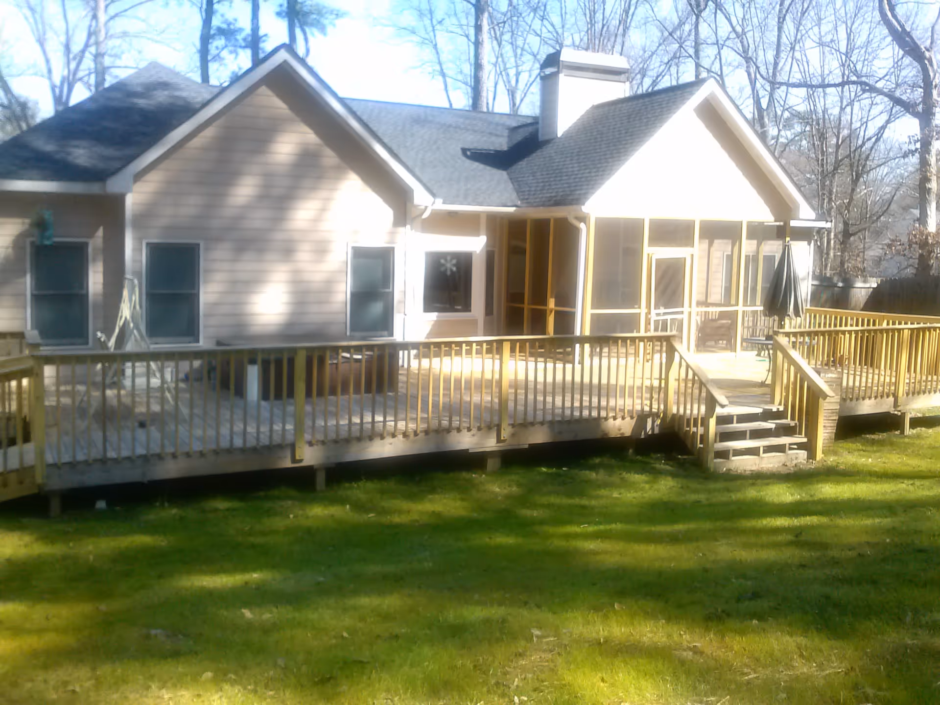 Rear exterior of a single-story house with a large wooden deck, screened porch, and grassy yard.