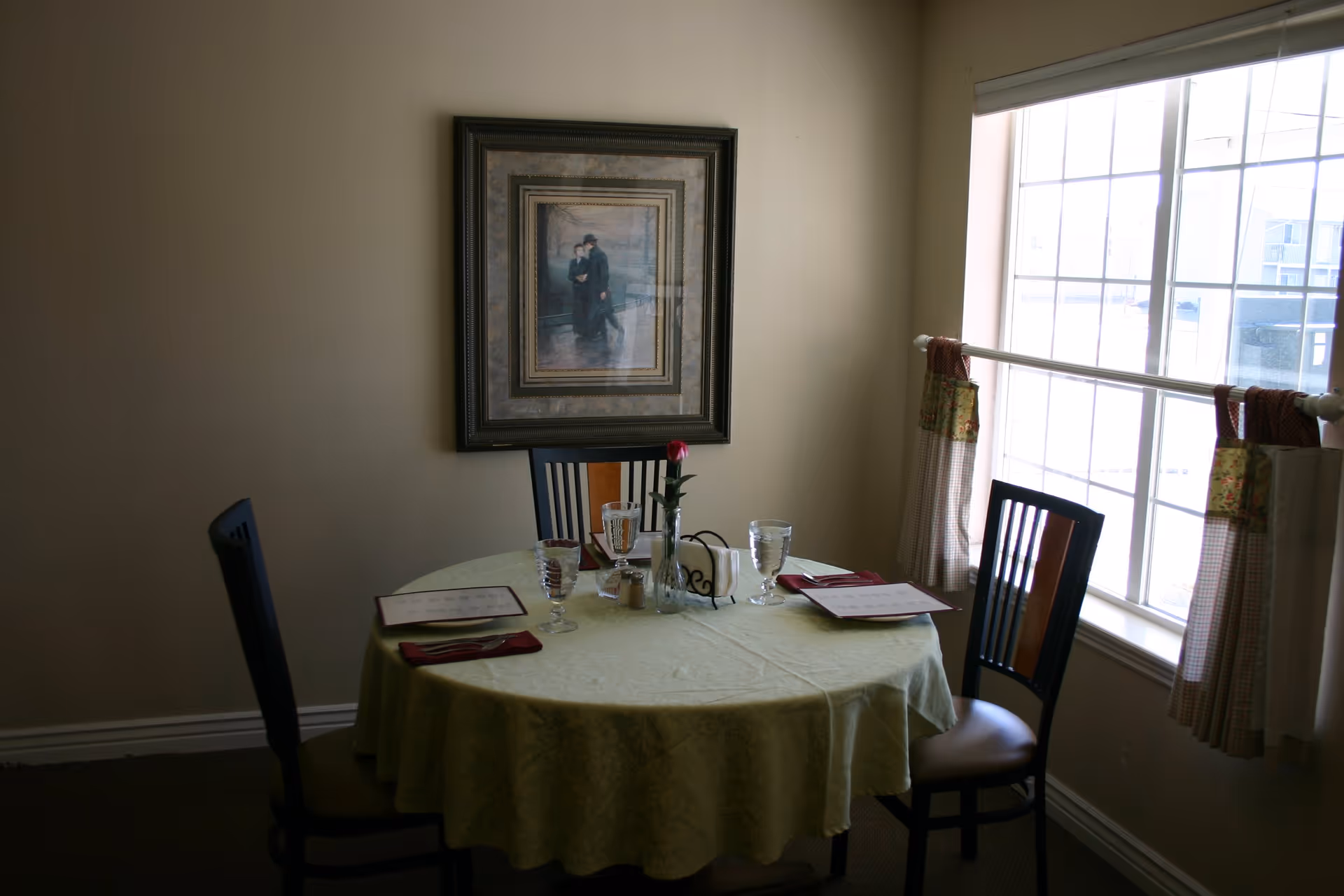 Small round dining table set for four by a window with chairs and framed artwork on the wall.