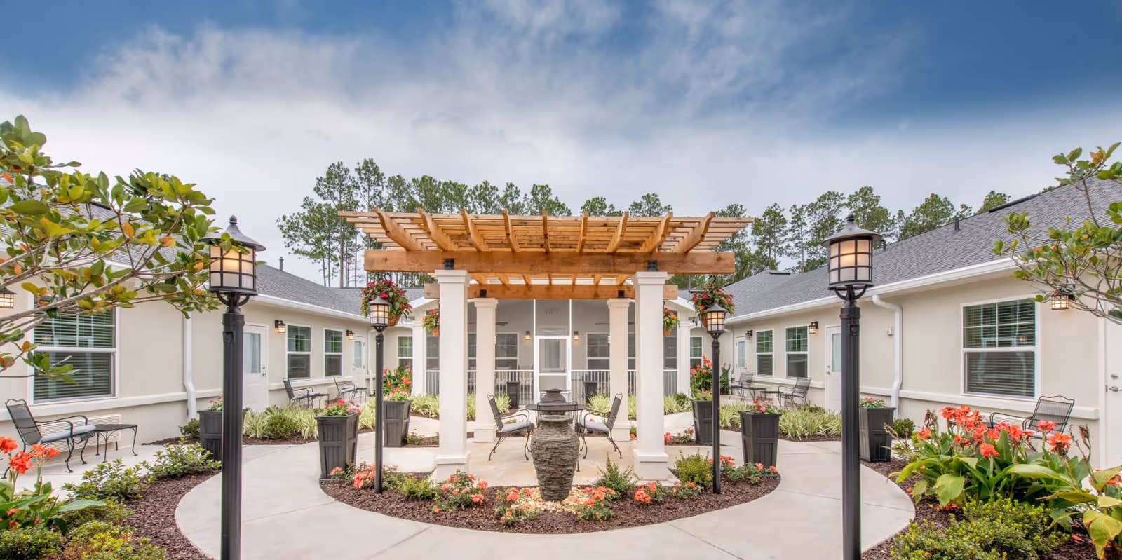 A beautifully landscaped courtyard at The Addison of Oviedo featuring a wooden pergola, decorative stone fountain, and seating areas surrounded by vibrant flowers and greenery.