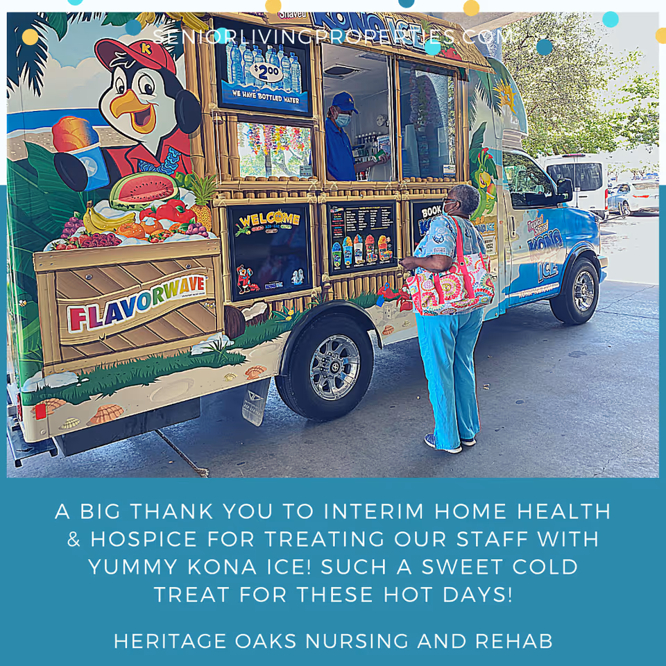 A woman wearing a mask and carrying a colorful bag stands at a Kona Ice truck window, where a man wearing a mask serves shaved ice. The truck is decorated with tropical and fruit-themed graphics, including a cartoon penguin and various fruits. The scene takes place outdoors on a sunny day.
