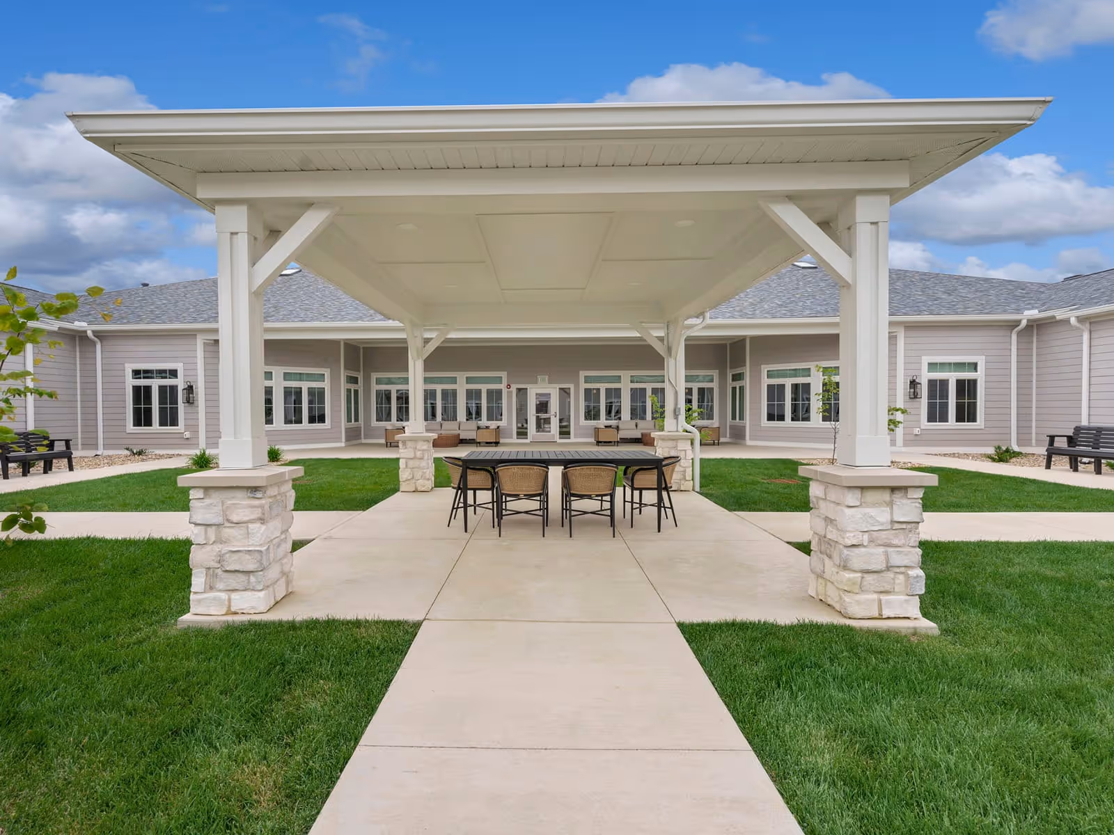 Covered outdoor pavilion with a table and chairs in the courtyard of a single-story senior living building.