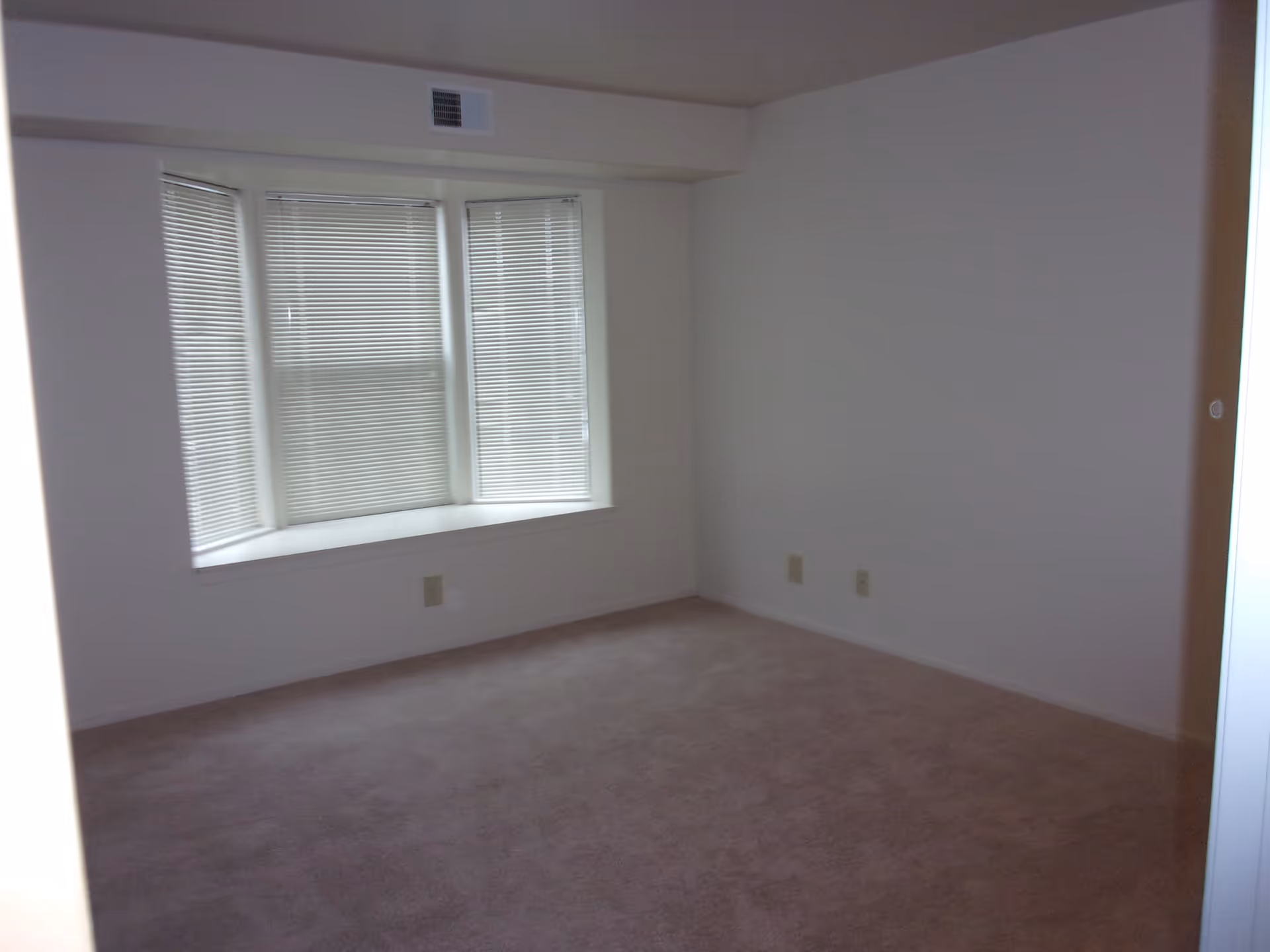 Empty carpeted room with a bay window and closed blinds.