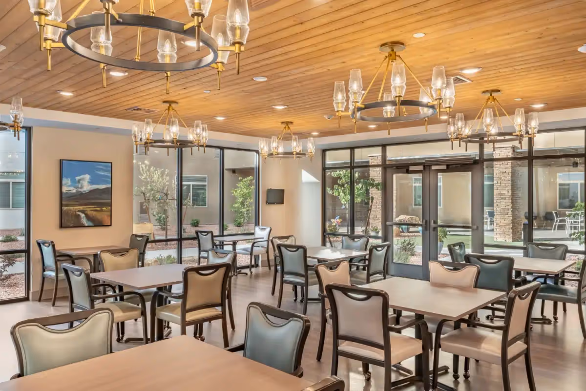 Bright dining room with multiple tables and chairs, large windows, and modern chandeliers.