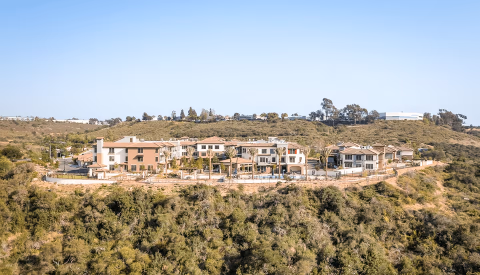 Aerial view of the Santianna Oakmont senior living complex on a hilltop with multiple Mediterranean-style buildings, a pool area, and surrounding vegetation.