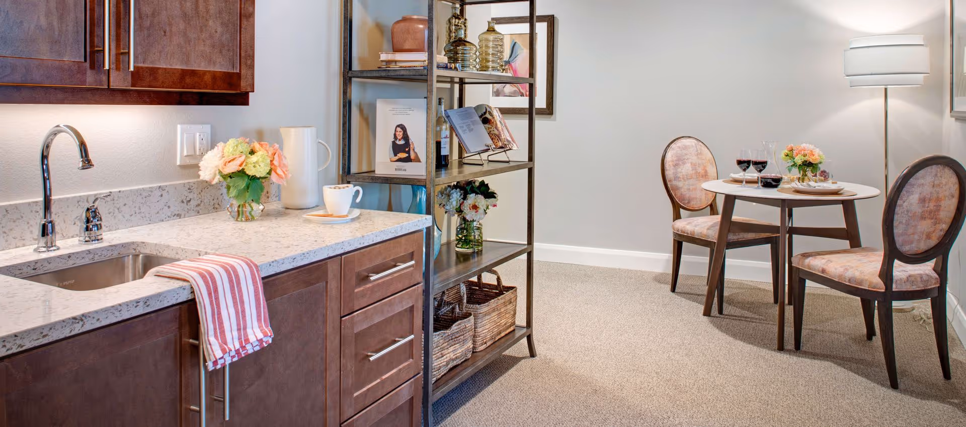 Small kitchenette with a granite countertop and sink, a shelving unit, and a round dining table with two chairs in the adjoining space.