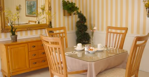 A dining room with a glass table, four wooden chairs, and a sideboard along striped walls.