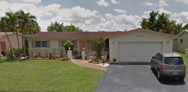 Front exterior of Paradise Villas Retirement with lawn, palm trees, and a parked SUV.