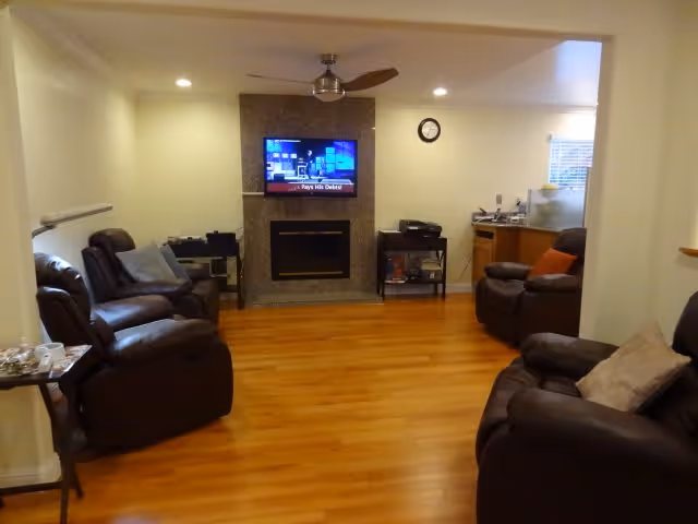 Cozy living room with hardwood floors, several leather recliners arranged around a central fireplace and a wall-mounted TV.