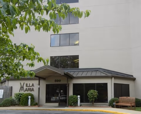 Exterior view of Villa Maria senior living facility entrance with glass doors and landscaping.