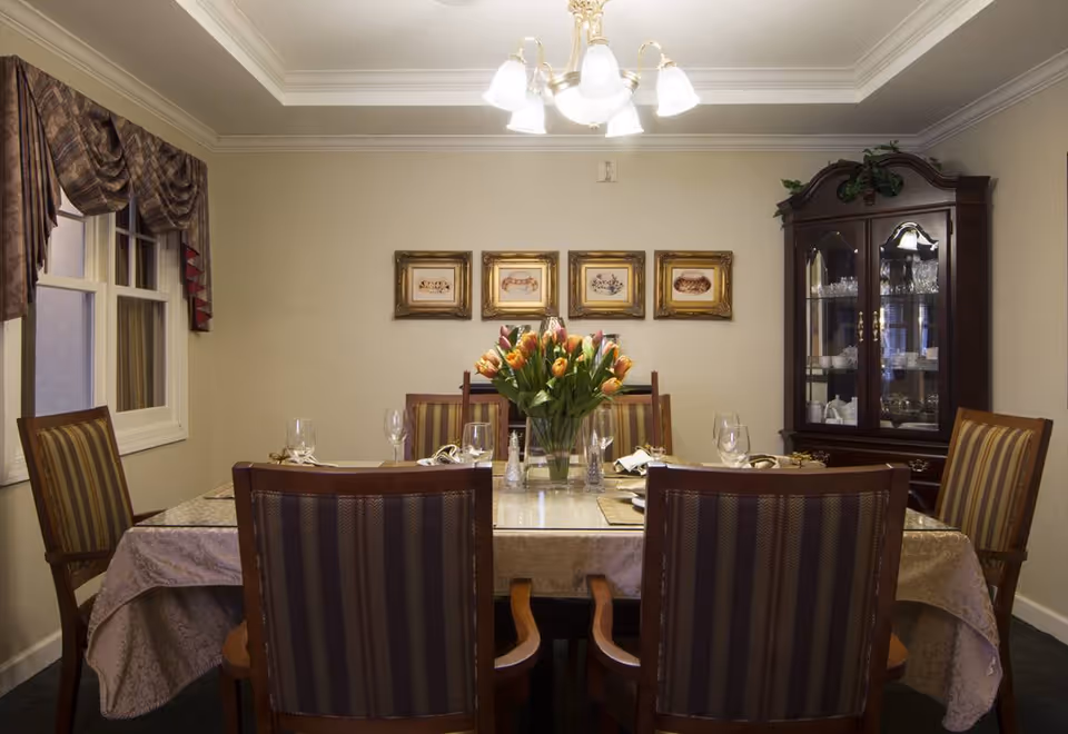 Formal dining room with a set table, vase of tulips, striped chairs, a china cabinet and framed artwork on the wall.