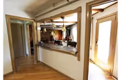 Hallway and open interior showing a pass-through counter to a kitchen/dining area, hardwood floors, and a glass exterior door.