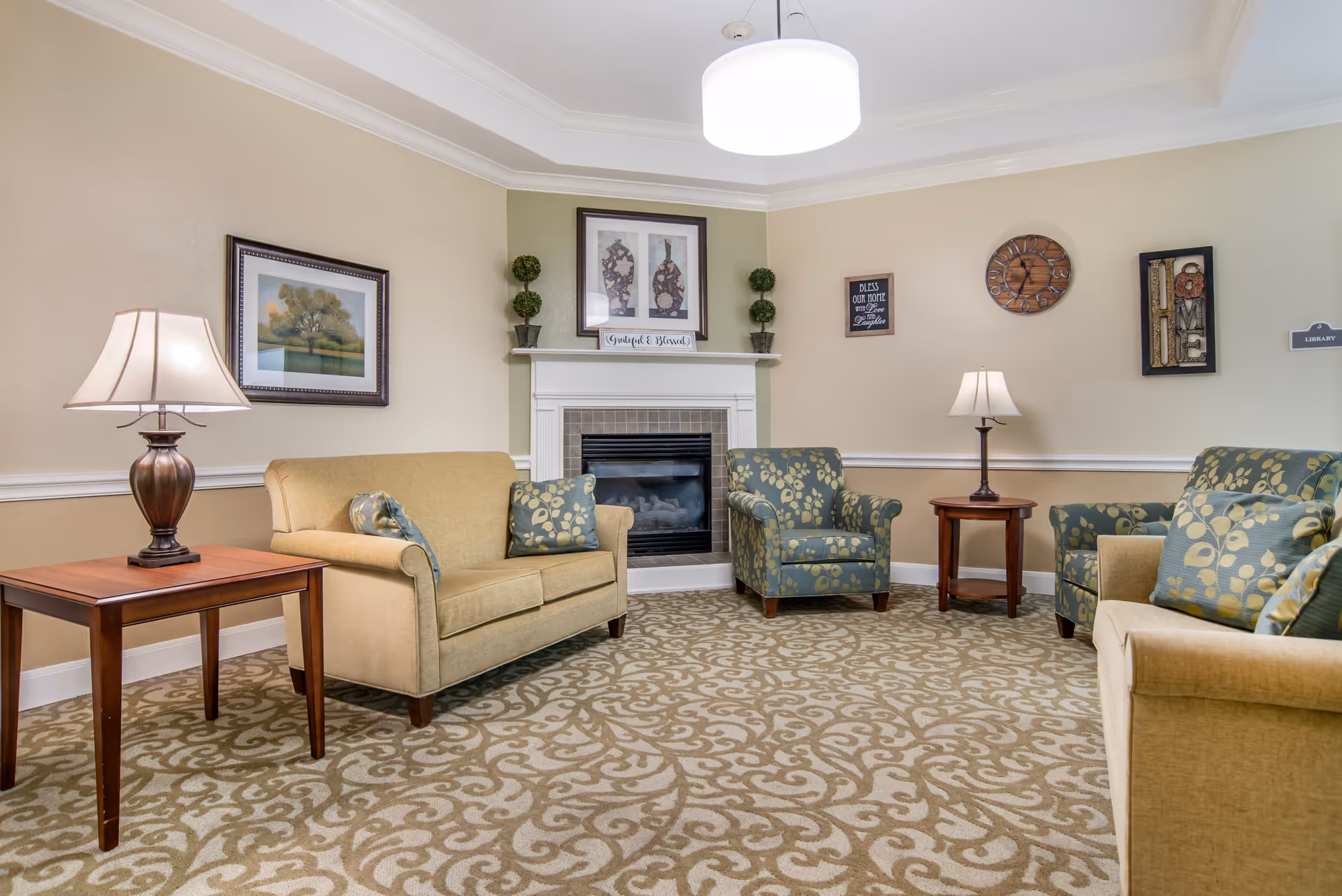 A cozy living room with sofas and armchairs arranged around a central fireplace and side tables with lamps.