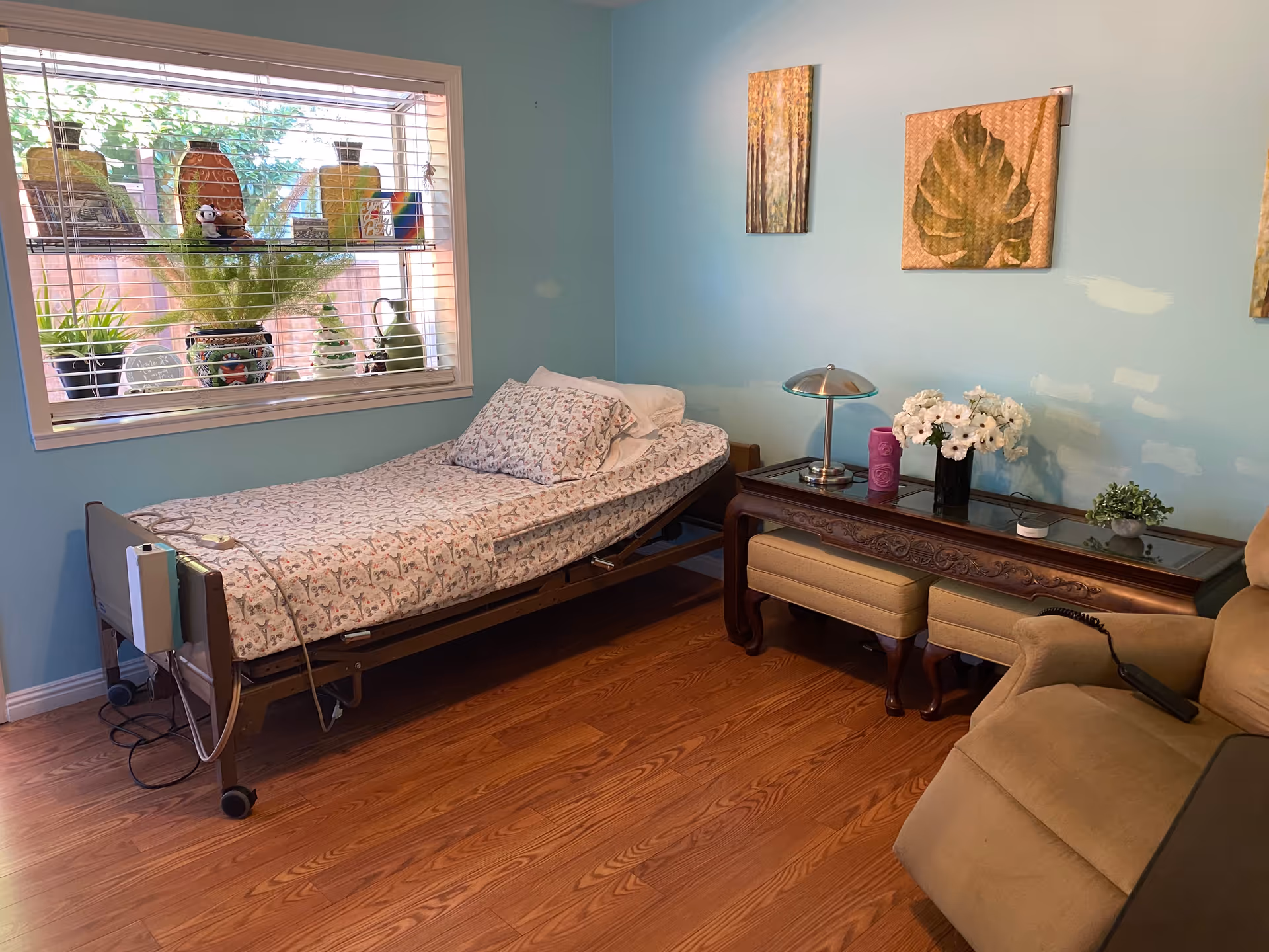 Blue-walled bedroom with an adjustable hospital bed, window blinds, and a glass-topped console.