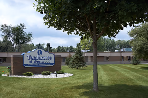 Exterior view of the Medilodge of Westwood facility showing a single-story building with a large sign in front that reads 'Tendercare of Westwood Skilled Nursing & Rehabilitation Center,' surrounded by green grass, trees, and a partly cloudy sky.