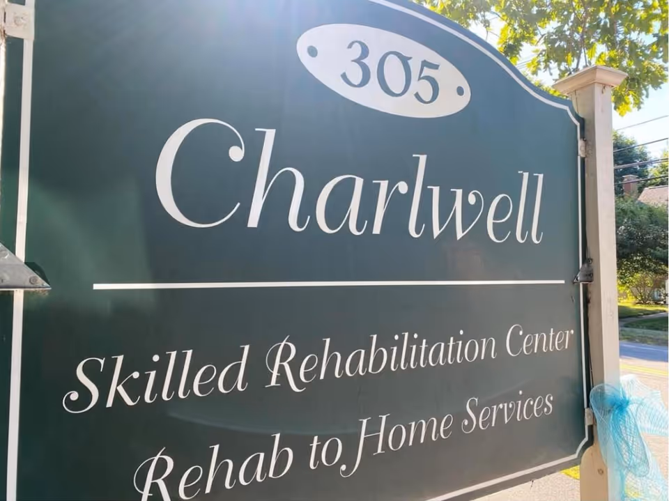 Outdoor sign for Charlwell Skilled Rehabilitation Center with the address number 305, indicating skilled rehabilitation and rehab to home services, mounted on white posts with trees and a street in the background.