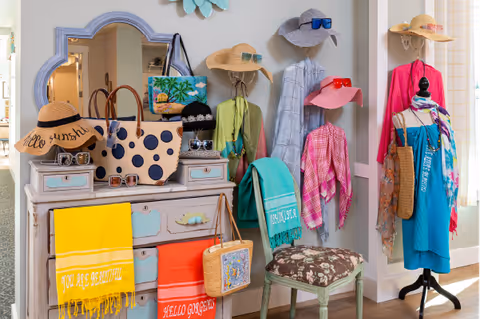 Colorful boutique-style interior display of hats, scarves, bags and accessories arranged on a dresser, wall hooks, and a mannequin.