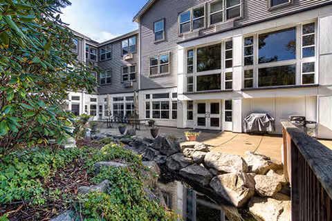 Exterior courtyard of a multi-story building with large windows, a paved patio and grill, and a landscaped rock pond.