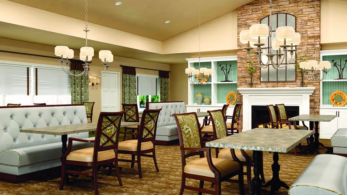 A cozy dining room with multiple tables and chairs arranged neatly. The room features cushioned bench seating along the walls, patterned curtains on the windows, and a stone fireplace with a mirror above it. Elegant chandeliers hang from the ceiling, and decorative vases and plates are displayed on built-in shelves.