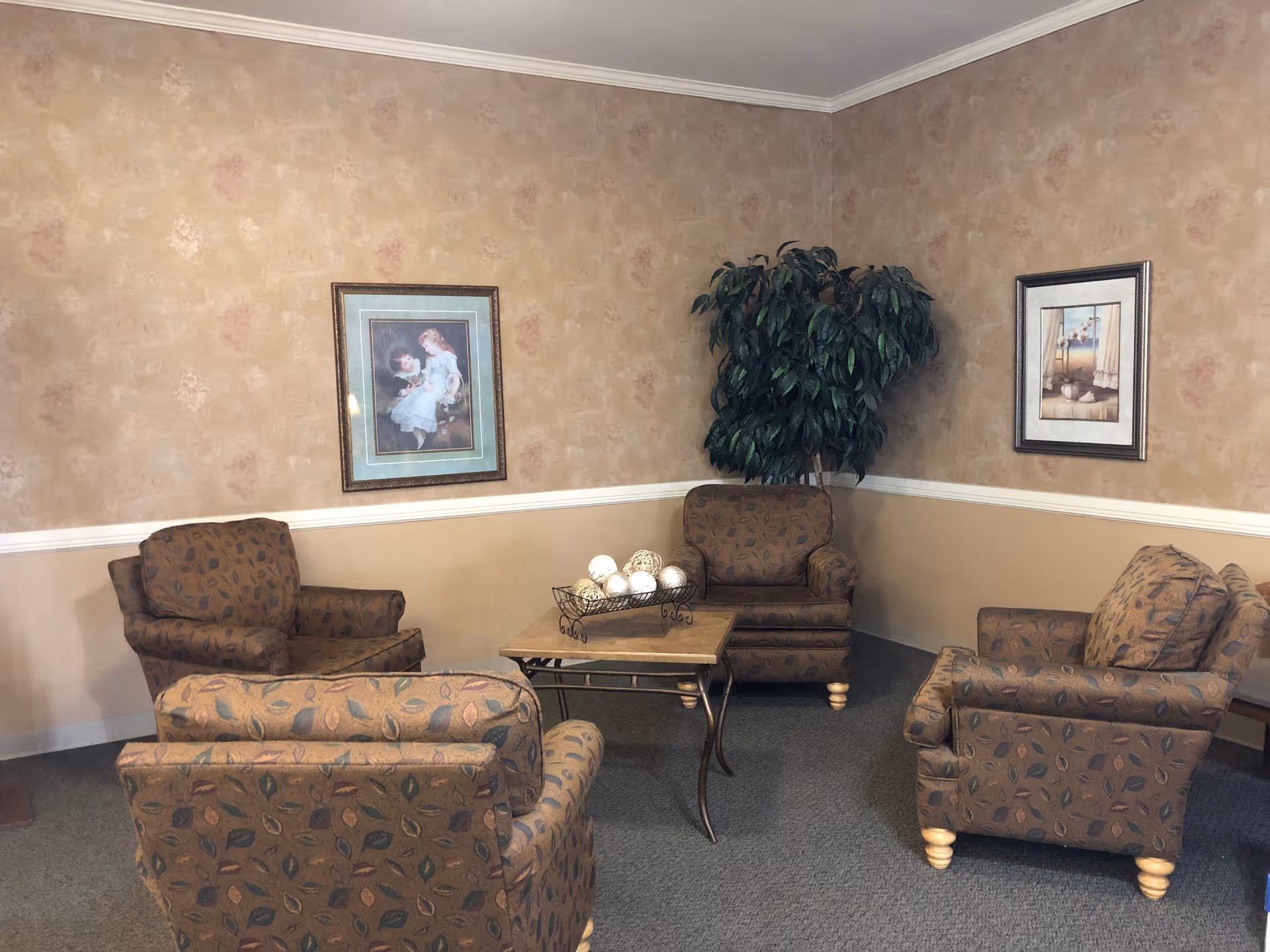 A cozy seating area with two patterned chairs, a table, decorative items, and framed artwork on the walls.