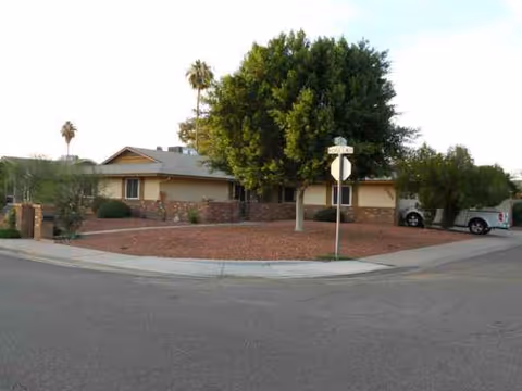 Single-story beige assisted living home on a street corner with red mulch yard.