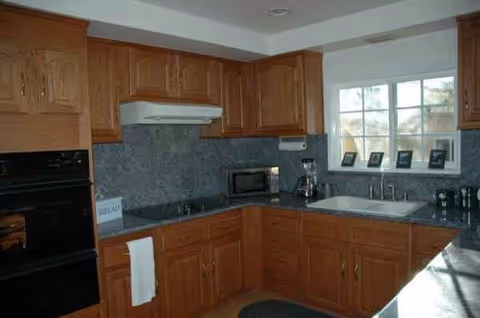 Wooden kitchen with granite countertops, appliances, and a double sink.