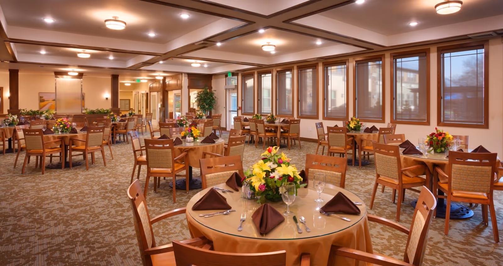 Spacious dining room with round tables set with place settings and floral centerpieces.