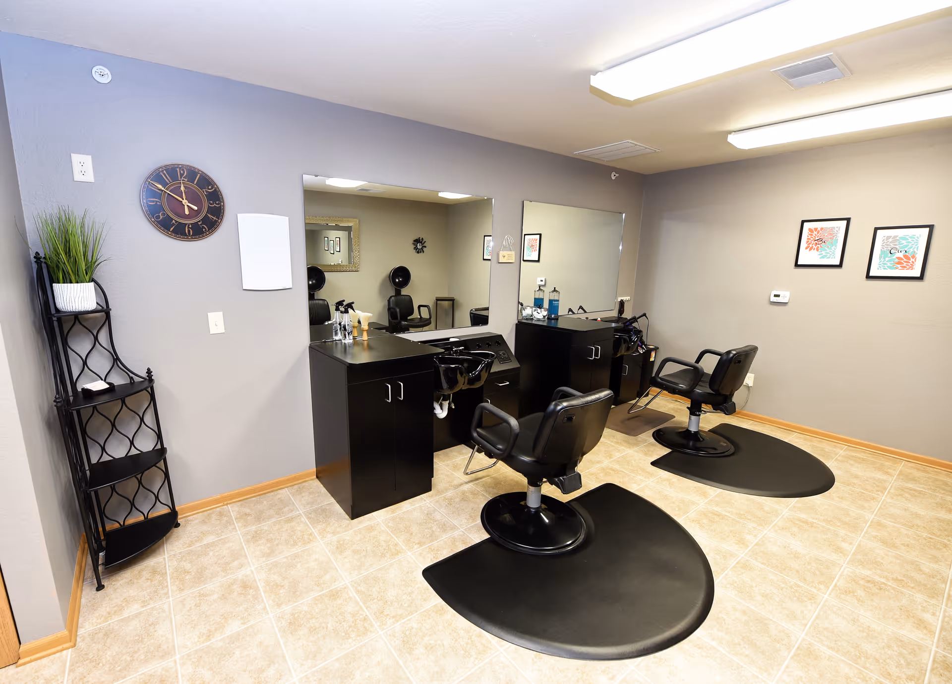Small salon-style room with two black styling chairs in front of mirrors, cabinets, and wall decor.