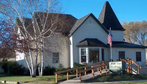 Exterior of Newcare Residence, a white building with a ramp and flag on a sunny day.