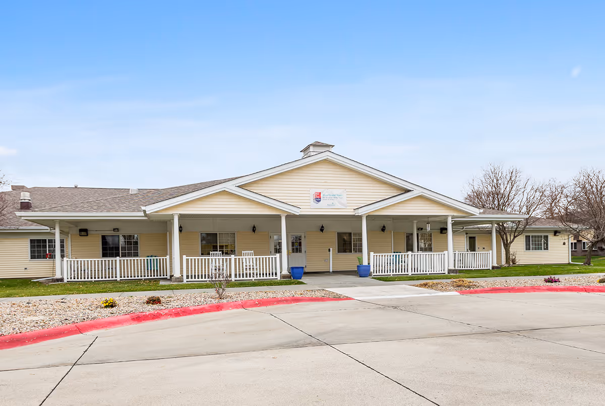 Single-story beige senior living facility with a covered front porch and white railing.