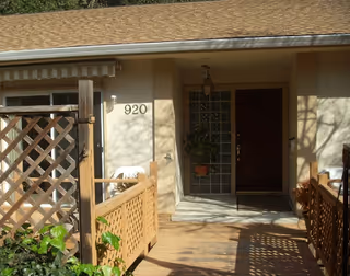 Senior living facility entrance with wooden porch, lattice railing, and potted plants.