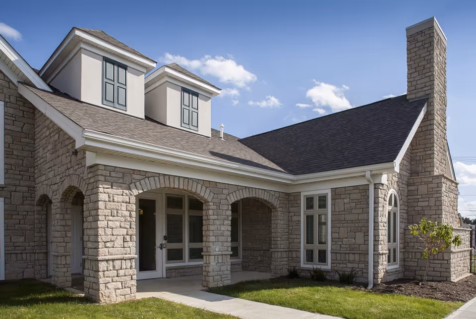 Exterior view of a stone building with arched doorways, multiple windows, a chimney, and a well-maintained lawn under a blue sky with some clouds.