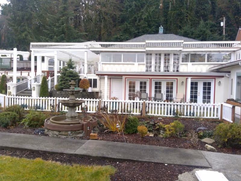 Front exterior of a two-story house with a white picket fence, garden fountain, and an upper covered veranda.
