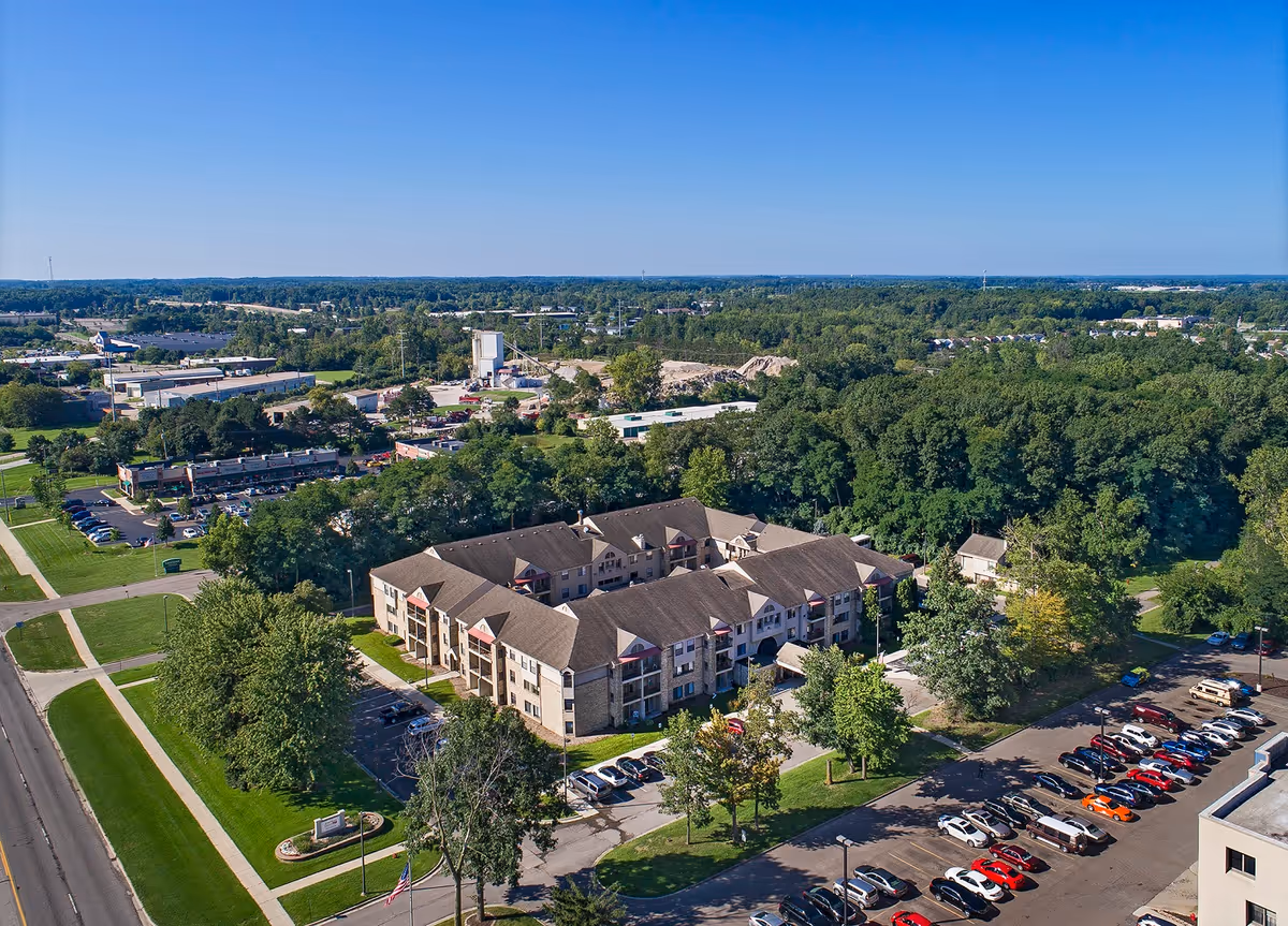 Aerial view of a multi-story senior living building surrounded by parking lots, lawns, and trees.