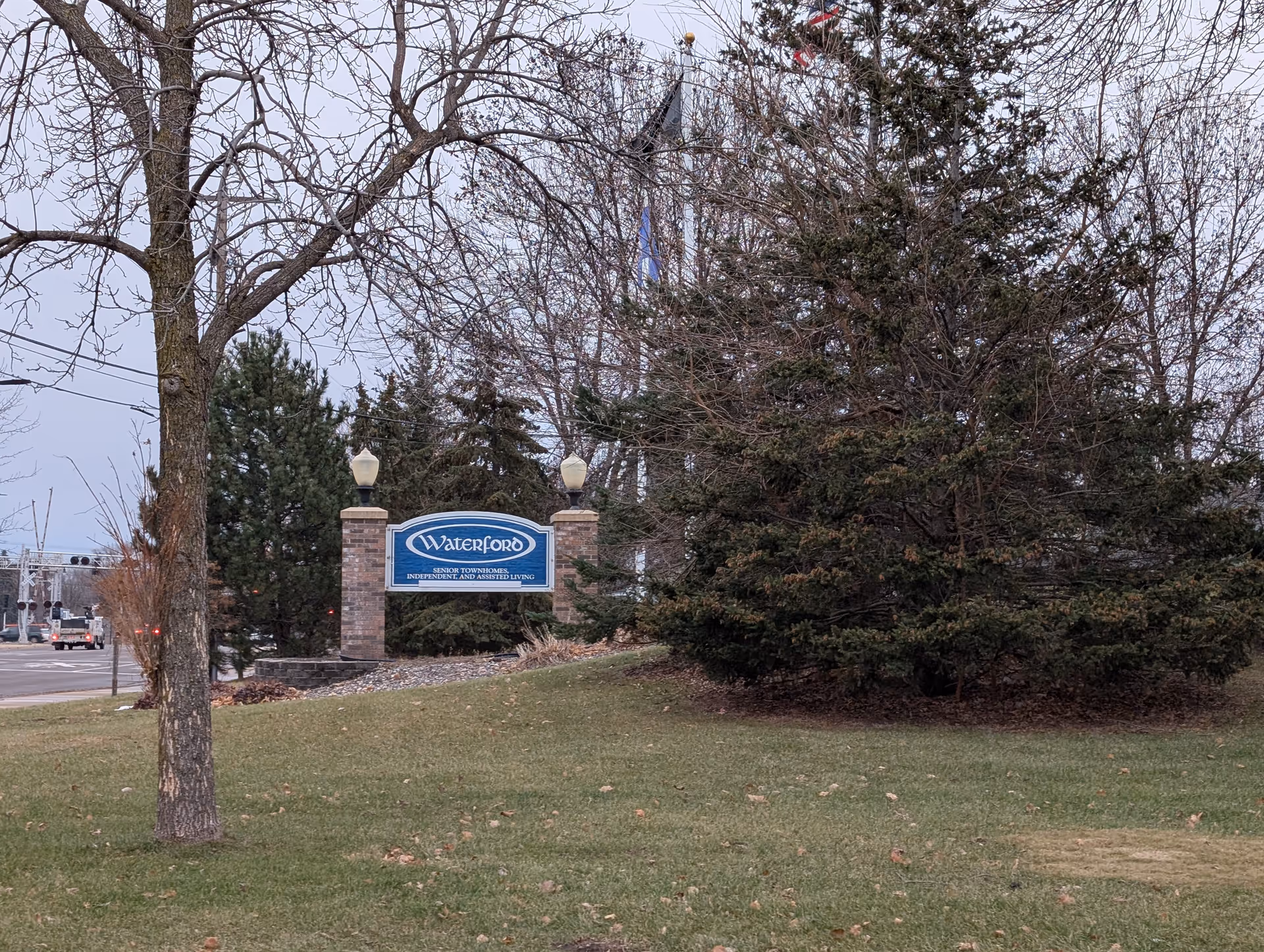 Brick entrance sign reading 'Waterford' at the front of a senior living property surrounded by trees and lawn.