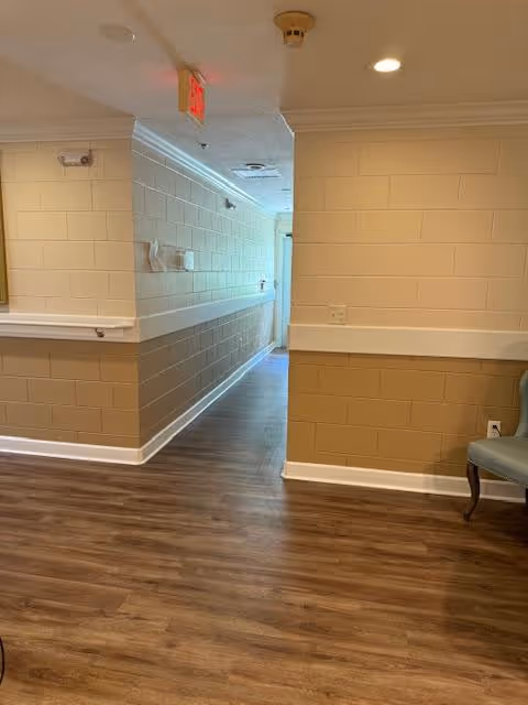 Interior hallway with wood-look flooring, beige half-height painted block walls, recessed ceiling lights, and an exit sign.