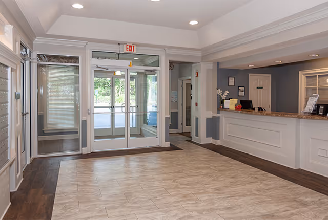 Entrance lobby with double glass doors, tile floor, and a reception desk to the right.