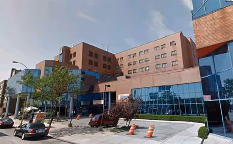Exterior view of Jamaica Hospital Medical Center building with glass facade and parked cars.