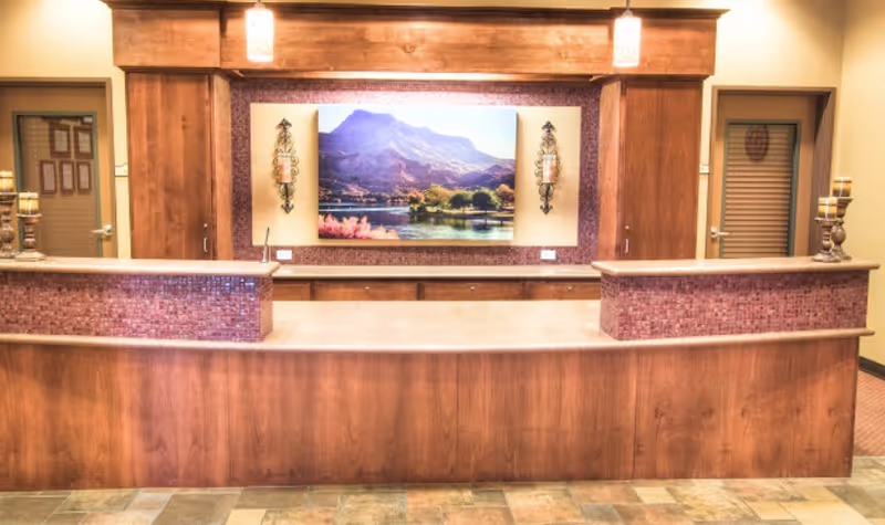 Wooden reception desk with mosaic-tiled counters and a large landscape painting on the wall behind it.