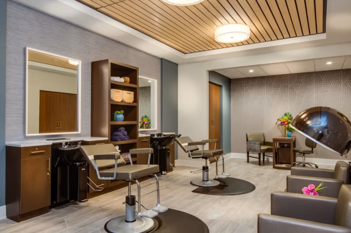Modern salon interior with styling chairs, mirrors, wash basins, and seating in a senior living facility.