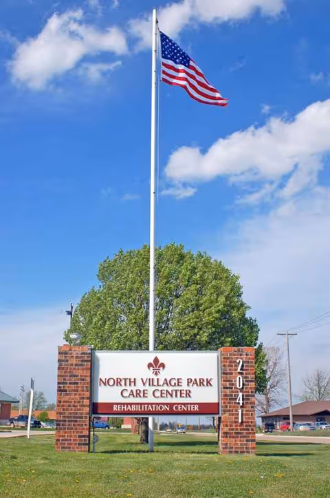 American flag atop a tall pole beside a brick sign for North Village Park Care Center
