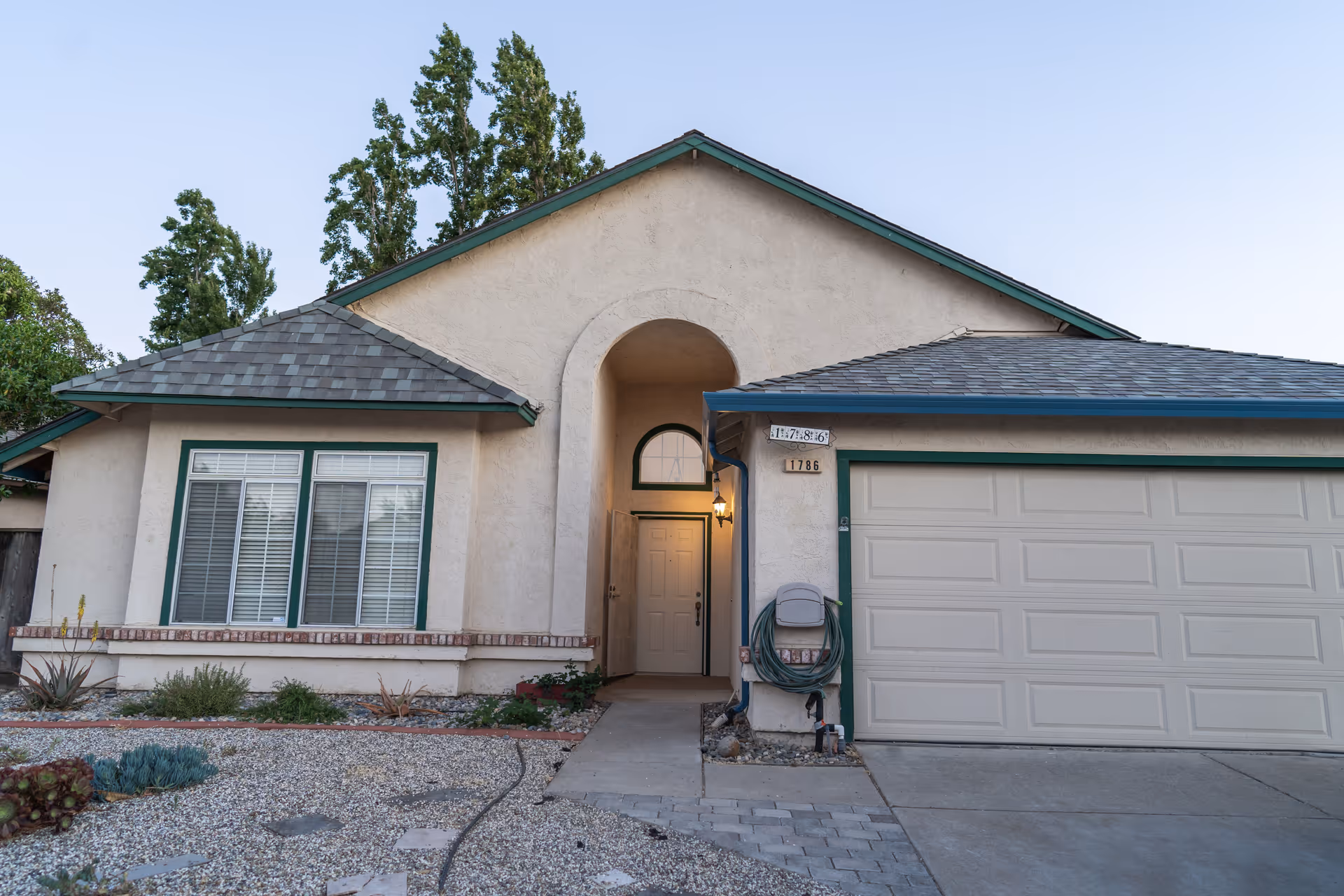 Front exterior of a single-story stucco house with an arched entryway, windows, and an attached garage.