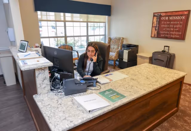A receptionist sits at a marble-front desk with a computer in a bright lobby area.