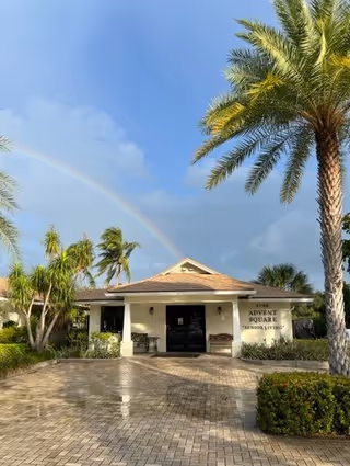 Front entrance of Advent Square Senior Living with palm trees and a rainbow overhead.