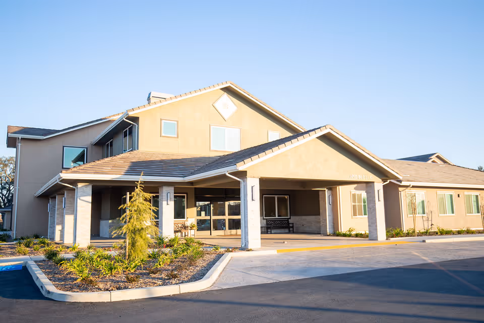 Front view of a beige senior living facility with a covered entrance and landscaped surroundings.