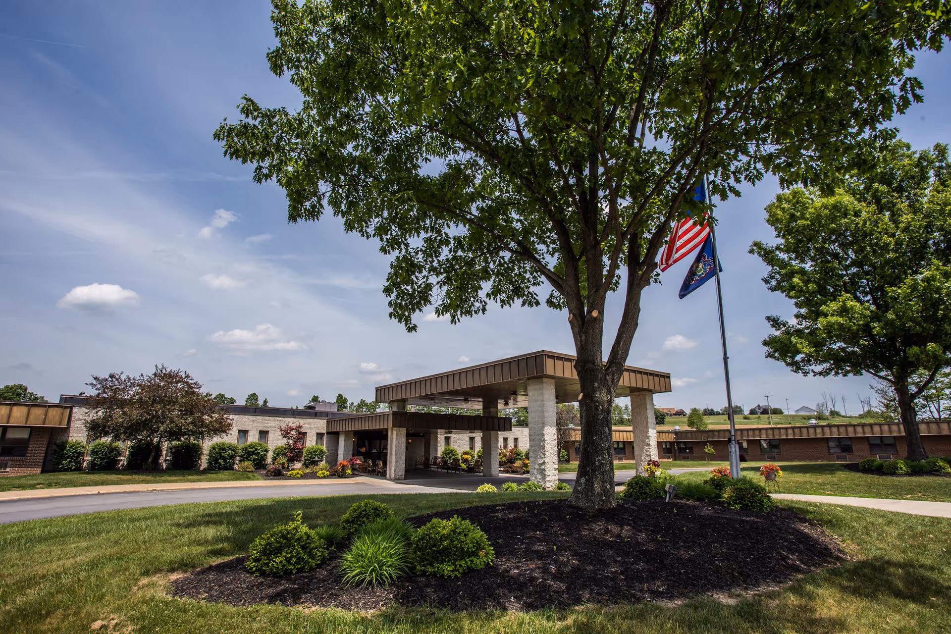 Exterior view of Clarview Nursing & Rehab Center showing a single-story building with a covered entrance, surrounded by well-maintained landscaping including trees, bushes, and a grassy area under a partly cloudy sky.