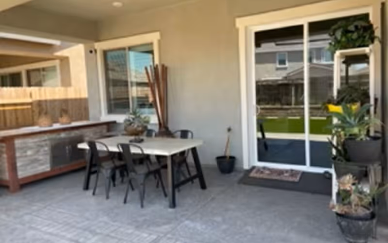 Covered patio with a dining table and chairs, potted plants, and a sliding glass door to the house.