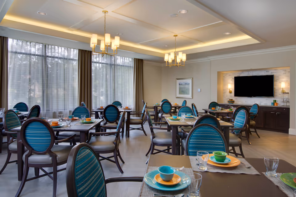 Dining room with several tables set with colorful dishes and teal-upholstered chairs under chandeliers.